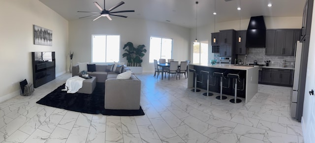 living area with a ceiling fan, recessed lighting, marble finish floor, and a towering ceiling