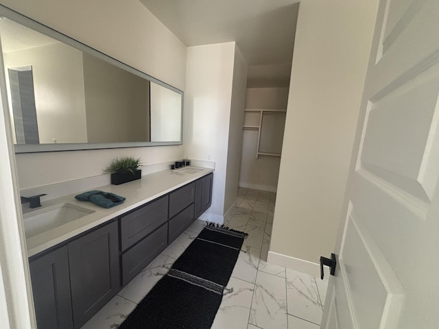 bathroom with baseboards, double vanity, a sink, a walk in closet, and marble finish floor