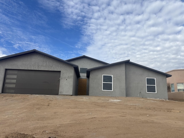 view of front of house featuring stucco siding, an attached garage, and dirt driveway