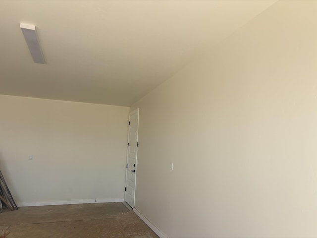 corridor featuring baseboards and unfinished concrete flooring