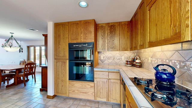 kitchen featuring black appliances, hanging light fixtures, decorative backsplash, and tile countertops