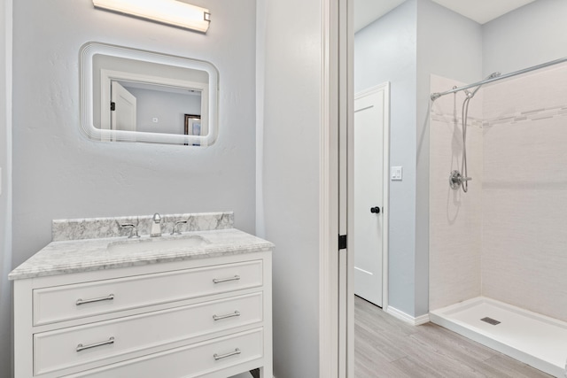 bathroom with tiled shower, hardwood / wood-style floors, and vanity