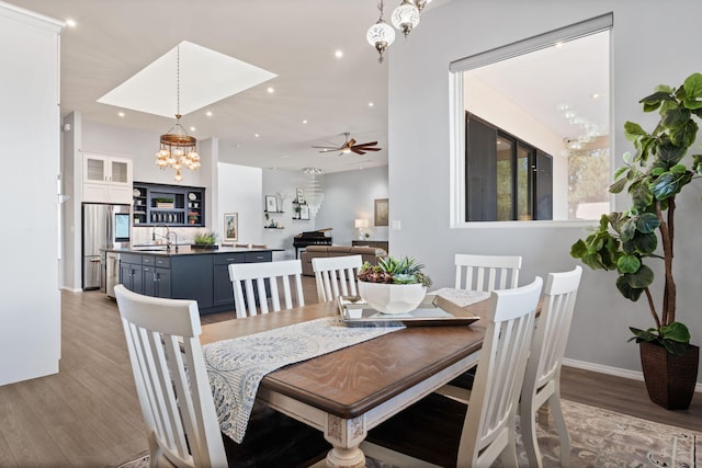 dining space with sink, ceiling fan with notable chandelier, and light wood-type flooring