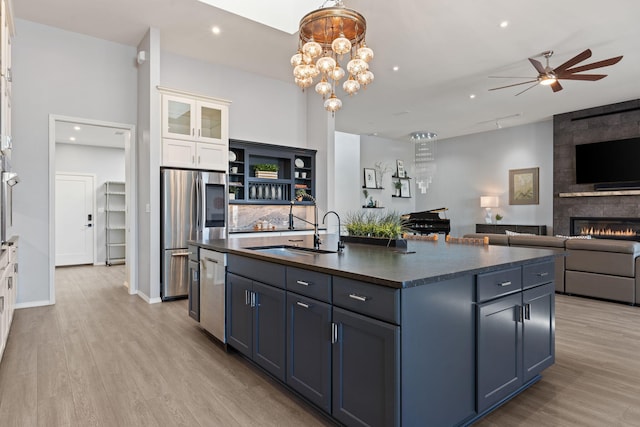 kitchen with a large fireplace, ceiling fan with notable chandelier, white cabinetry, sink, and a center island with sink