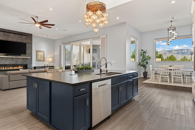 kitchen with a fireplace, ceiling fan with notable chandelier, dishwasher, sink, and an island with sink