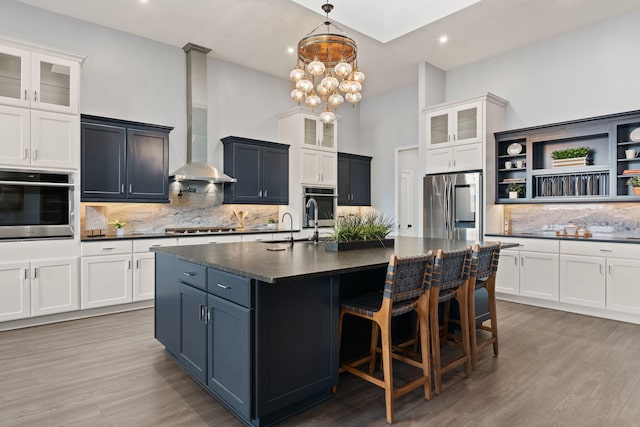 kitchen with backsplash, an inviting chandelier, appliances with stainless steel finishes, a center island with sink, and light hardwood / wood-style floors