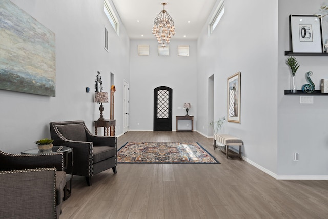 foyer with wood-type flooring, an inviting chandelier, and a towering ceiling