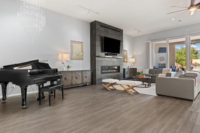 living room with a tiled fireplace, ceiling fan with notable chandelier, and wood-type flooring