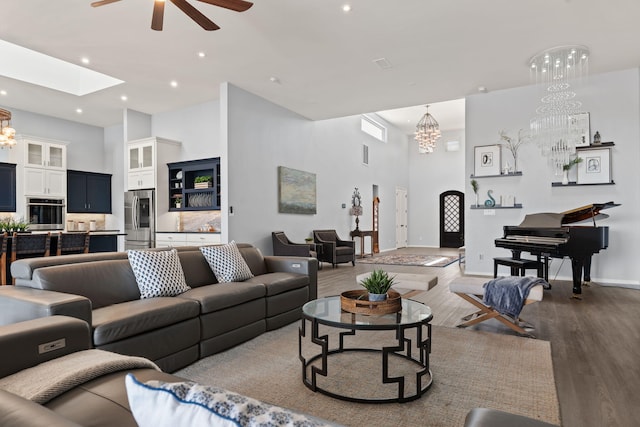 living room featuring ceiling fan with notable chandelier, light wood-type flooring, and a skylight