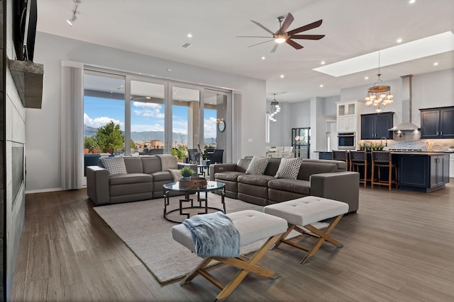 living room with a skylight, ceiling fan with notable chandelier, and hardwood / wood-style flooring