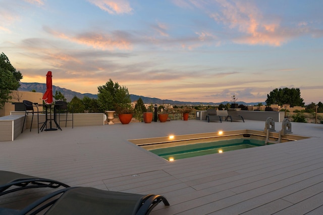 deck at dusk featuring a mountain view and a pool