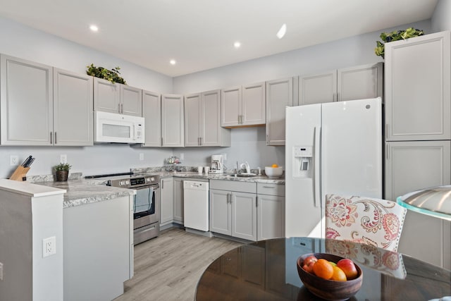 kitchen featuring light wood-type flooring, white appliances, light stone counters, and sink