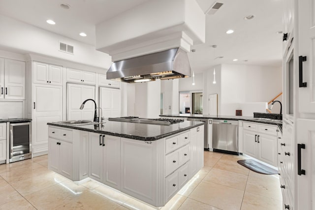 kitchen featuring visible vents, appliances with stainless steel finishes, a sink, beverage cooler, and wall chimney exhaust hood