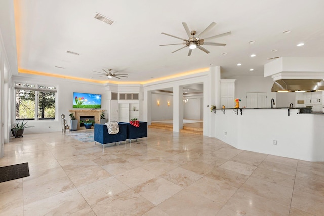 living area with a ceiling fan, a glass covered fireplace, visible vents, and recessed lighting