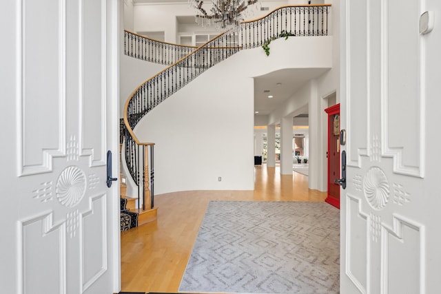 entryway with light hardwood / wood-style floors, a notable chandelier, and a towering ceiling