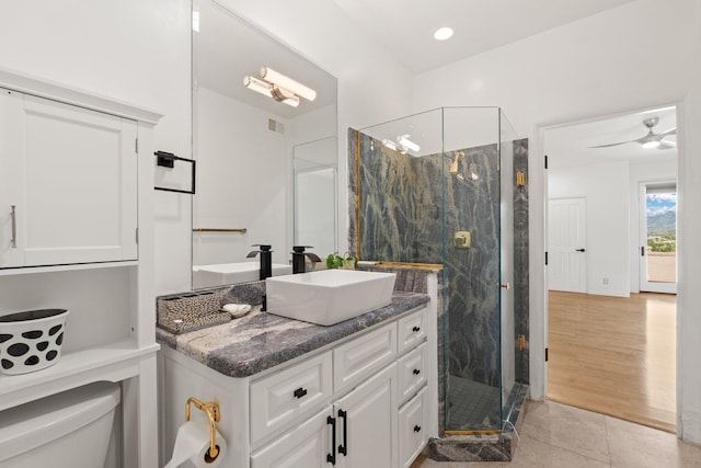 bathroom with a shower with door, vanity, toilet, tile patterned floors, and ceiling fan