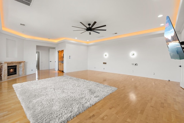 living area featuring a tray ceiling, a premium fireplace, visible vents, and light wood-style floors