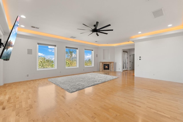 unfurnished living room with a tray ceiling, visible vents, a high end fireplace, ceiling fan, and light wood-type flooring