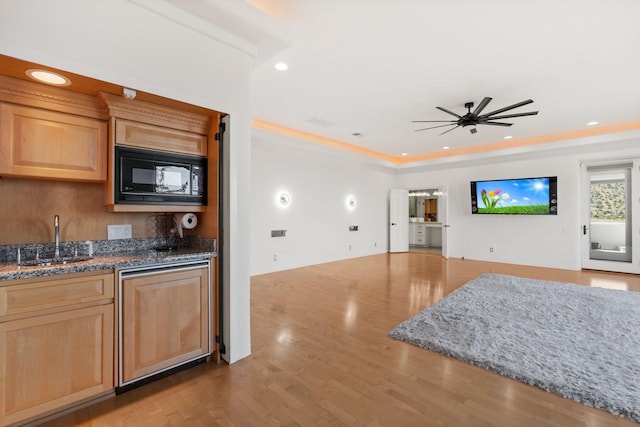 kitchen with dark stone counters, black microwave, a sink, and wood finished floors