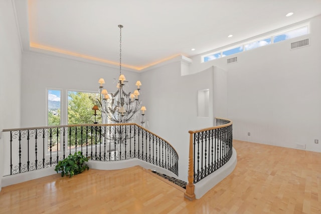 hallway with wood finished floors, an upstairs landing, visible vents, and a notable chandelier