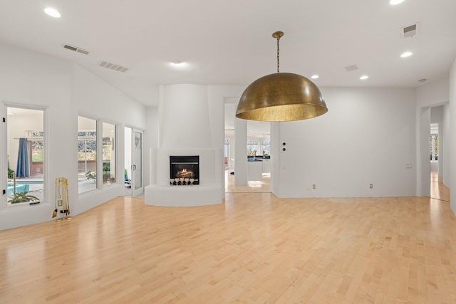 unfurnished living room featuring light wood-style floors, visible vents, and a lit fireplace