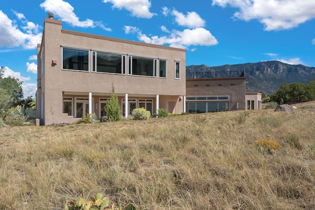 rear view of house featuring a chimney, a mountain view, and stucco siding