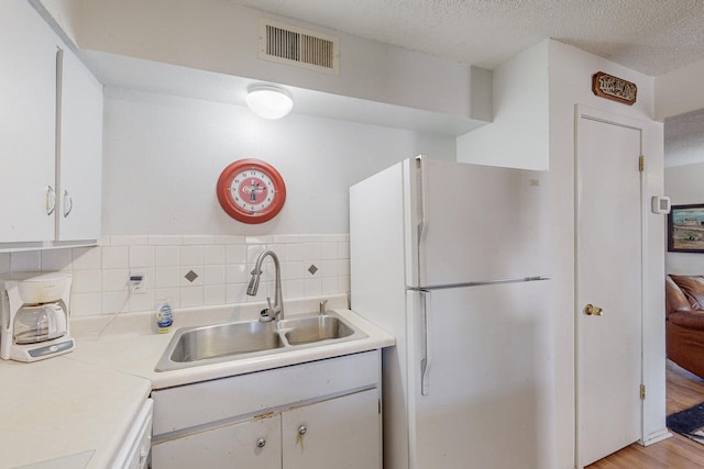 kitchen with white cabinetry, sink, backsplash, white appliances, and a textured ceiling