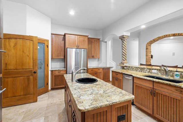 kitchen with decorative columns, stainless steel appliances, a center island with sink, and sink