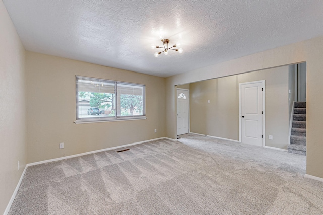 empty room with a textured ceiling, a chandelier, and carpet