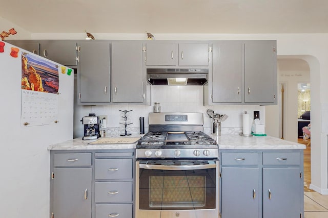 kitchen with gray cabinetry, light tile patterned floors, backsplash, and stainless steel gas range