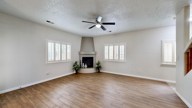 unfurnished living room with a fireplace, a textured ceiling, plenty of natural light, and light wood-type flooring