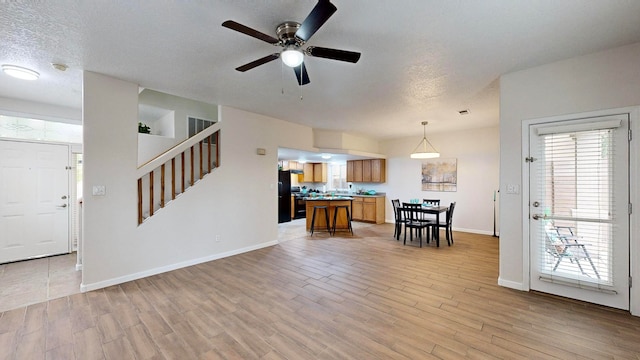 living room with a textured ceiling, light wood-type flooring, and ceiling fan