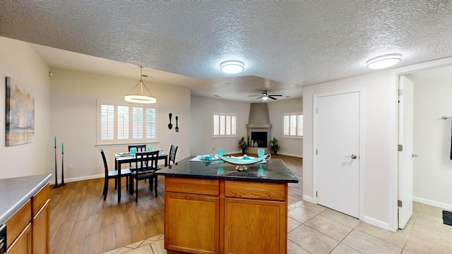 kitchen with a large fireplace, a textured ceiling, light wood-type flooring, a center island, and decorative light fixtures