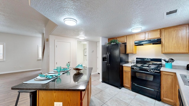 kitchen with black appliances, a kitchen island, a textured ceiling, light hardwood / wood-style floors, and a breakfast bar area