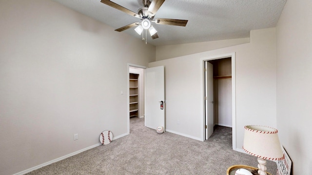 unfurnished bedroom with a walk in closet, a closet, ceiling fan, light carpet, and lofted ceiling