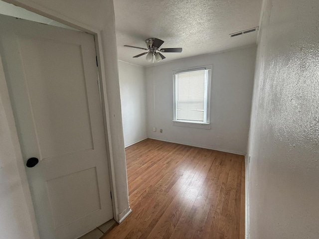 unfurnished room with ceiling fan, a textured ceiling, and light wood-type flooring