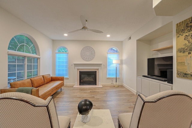 living area featuring a ceiling fan, a glass covered fireplace, visible vents, and light wood finished floors