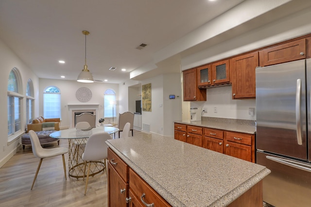 kitchen with visible vents, brown cabinets, stainless steel refrigerator, open floor plan, and a fireplace