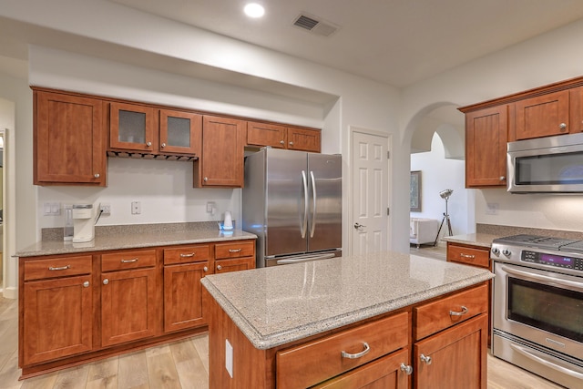 kitchen featuring visible vents, brown cabinetry, light wood-style flooring, light stone counters, and stainless steel appliances