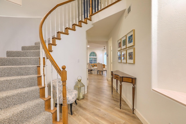 stairs featuring visible vents, a high ceiling, baseboards, and wood finished floors