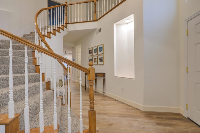 staircase featuring baseboards, a high ceiling, visible vents, and wood finished floors