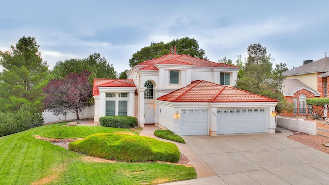 mediterranean / spanish-style home featuring a tile roof, stucco siding, an attached garage, a front yard, and driveway