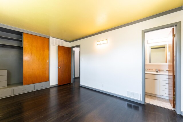 unfurnished bedroom featuring dark wood-type flooring, a closet, and ensuite bathroom