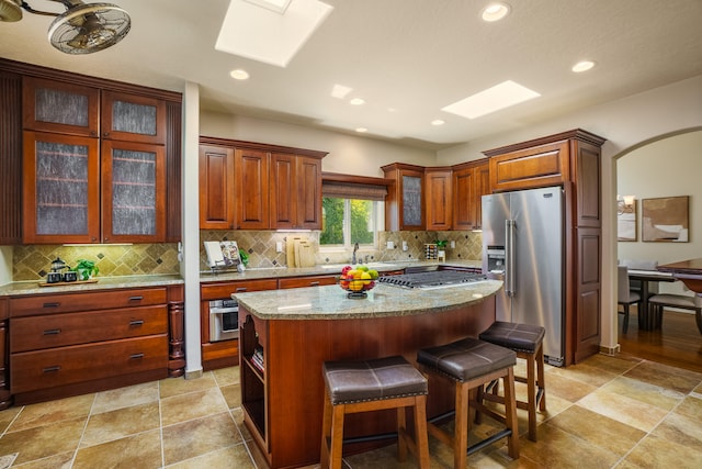 kitchen featuring a kitchen island, light stone countertops, a kitchen bar, stainless steel appliances, and a skylight