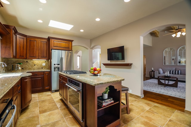 kitchen featuring a center island, appliances with stainless steel finishes, light stone countertops, light hardwood / wood-style floors, and ceiling fan