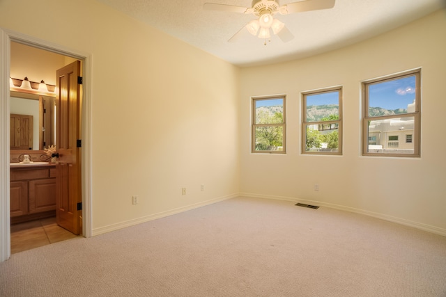 unfurnished bedroom with ceiling fan, light colored carpet, ensuite bathroom, and sink