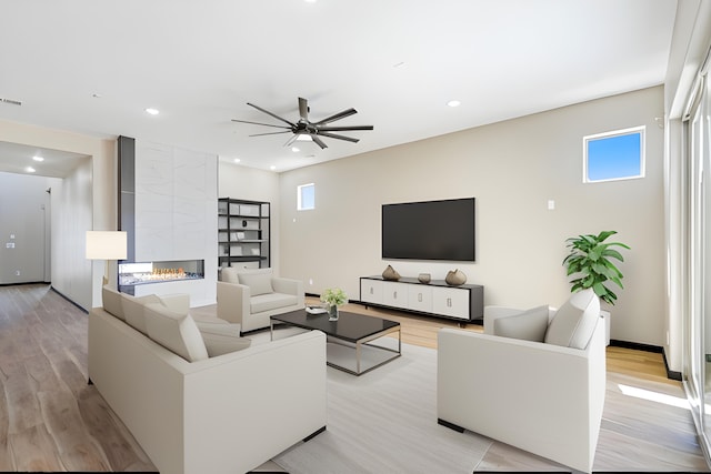 living room with a tiled fireplace, light hardwood / wood-style flooring, and ceiling fan