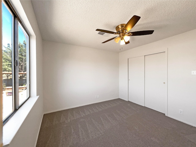 unfurnished bedroom with a textured ceiling, dark colored carpet, ceiling fan, and a closet