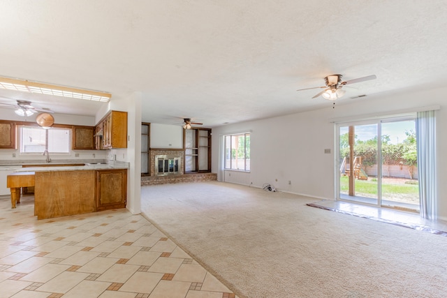 kitchen with a fireplace, ceiling fan, light colored carpet, and kitchen peninsula