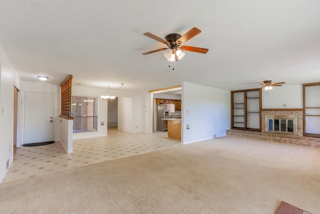 unfurnished living room featuring a brick fireplace, light colored carpet, a textured ceiling, and ceiling fan with notable chandelier